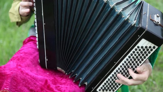 Closeup detail of hands playing a black accordion instrument outdoors summer