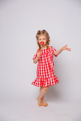 Funny smiling baby girl in a summer dress on a white background full-length . Baby girl with a lip accessory on a stick.