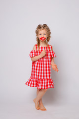 Funny smiling baby girl in a summer dress on a white background full-length . Baby girl with a lip accessory on a stick.