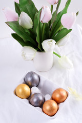 Greeting Easter card with handmade painted bright eggs and bouquet of fresh tulips flowers on a light textile background.