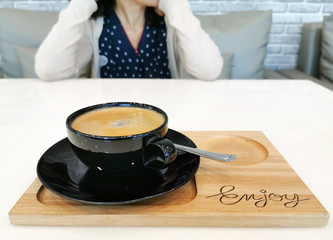 black coffee cup on wood tray, on white table and blur woman sitting opposite