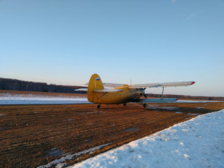 Yellow old biplane plane on a dirt runway in winter on a Sunny day with blue sky and white snow