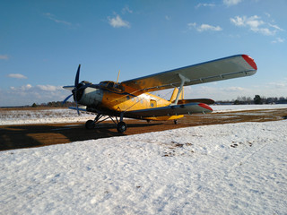 Yellow old biplane plane on a dirt runway in winter on a Sunny day with blue sky and white snow