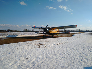 Yellow old biplane plane on a dirt runway in winter on a Sunny day with blue sky and white snow