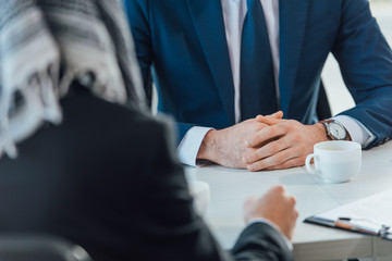 cropped view of businesspeople having meeting in office with coffee cups