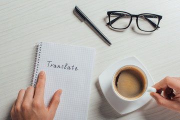 cropped view of translator with notepad, pen, eyeglasses and cup of coffee