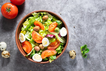 Fresh organic green salad with tomatoes, olives and quail eggs on dark stone table with copy space for your text. Healthy food concept.