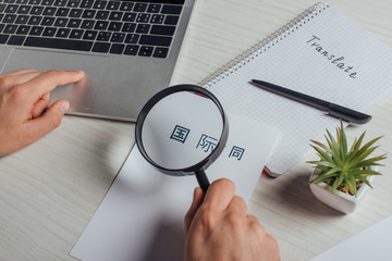 cropped view of translator working with hieroglyphics, laptop and magnifying glass