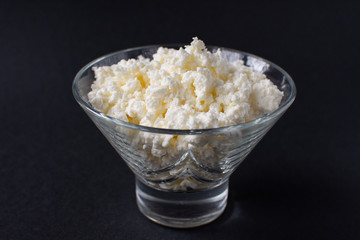 Homemade rustic crumbly cottage cheese on a black background.