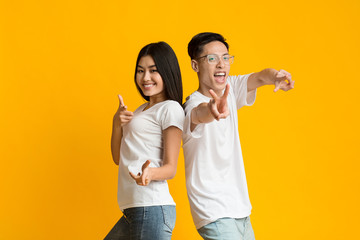 Joyful asian couple having fun over yellow background