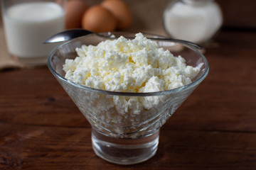 Homemade rustic crumbly cottage cheese with milk on a wooden background. Still-life.