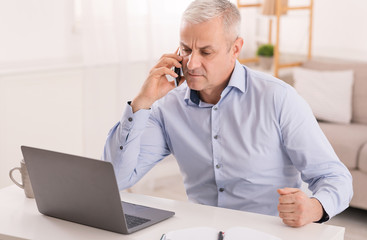 Serious mature man talking on mobile phone at office