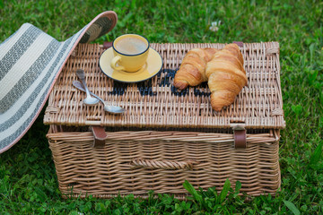 Wicker picnic basket on grass with food and coffee