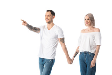 young tattooed couple holding hands while man pointing with finger away isolated on white