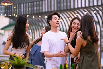 Group of people are talking and smiling together with happy moment in the evening time of rooftop restaurant party, concept of friendship, relation and modern lifestyle.