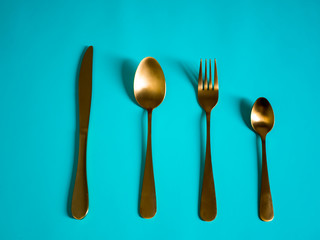 set of tableware. Knife fork spoon made of yellow metal imitating gold on a blue background