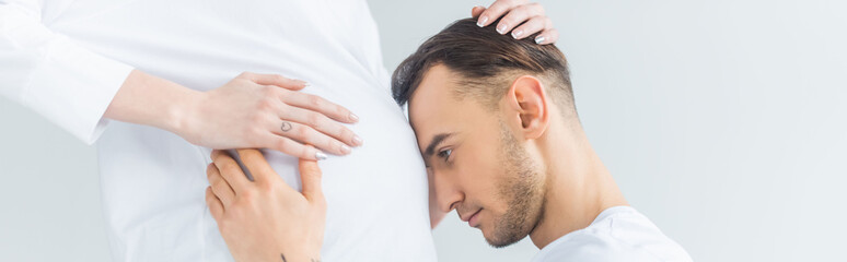 Fototapeta na wymiar side view of young man touching belly of pregnant wife isolated on grey, panoramic shot