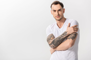 serious handsome young tattooed man with crossed arms isolated on white