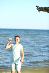 Fototapeta na wymiar handsome boy in shorts and a t-shirt teenager launches a kite on the sky on the seashore in summer