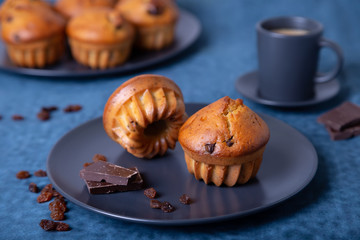 Muffins with chocolate and raisins. Homemade baking. In the background is a plate with muffins and a cup of coffee. Blue background. Close-up.