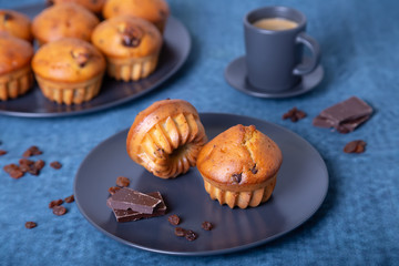 Muffins with chocolate and raisins. Homemade baking. In the background is a plate with muffins and a cup of coffee. Blue background. Close-up.