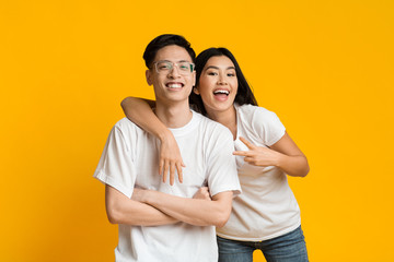 Portrait of joyful asian couple posing over yellow background