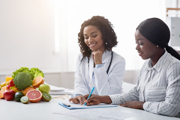 Obraz na płótnie Canvas Black woman patient of nutritionist filling form during consultation