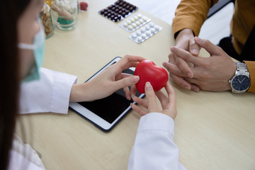 Top view of a nutritionist doctor is educating a young businessman about taking heart disease and supplements via tablet in the consultation room. Concept about health care and good health.