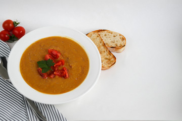 Vegetable soup with lentils on a white background. Served with chopped cherry tomatoes and herbs. Nearby are pieces of ciabatta. Raw groats in the background. Vegetarian dish.