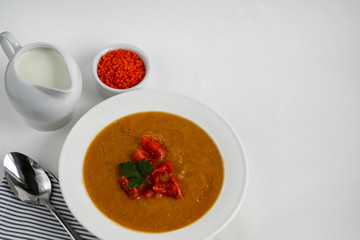 Vegetable soup with lentils on a white background. Served with chopped cherry tomatoes and herbs. Nearby are pieces of ciabatta. Raw groats in the background. Vegetarian dish.