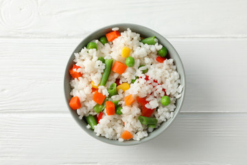 Bowl of delicious rice with vegetables on wooden background, top view