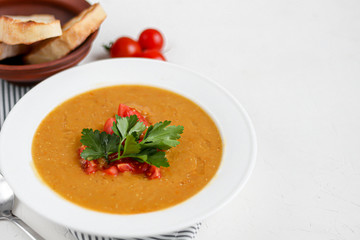 Vegetable soup with lentils on a white background. Served with chopped cherry tomatoes and herbs. Nearby are pieces of ciabatta. Raw groats in the background. Vegetarian dish.