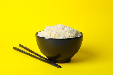 Bowl with boiled rice and chopsticks on yellow background, space for text
