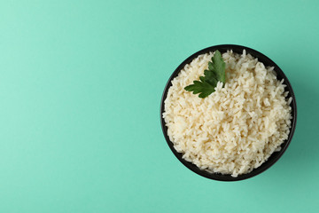 Bowl with boiled rice and parsley on mint background, top view