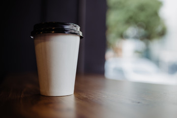 A white to-go coffee cup on a table near a window
