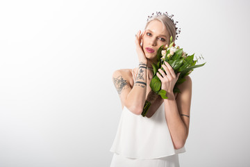 portrait of beautiful tattooed bride posing with floral bouquet on white