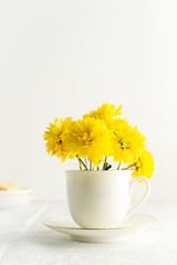 Small bouquet of yellow spring flowers in white cup. Closeup view