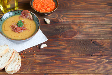 Vegetable soup with lentils on a wooden background. Served with chopped cherry tomatoes and herbs. Nearby are pieces of ciabatta. Raw groats in the background. Vegetarian dish.
