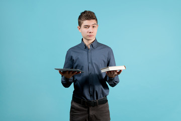 A teenager in a blue shirt holds a tablet and a book in front of him