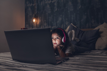 little girl lying in bed focused on a computer