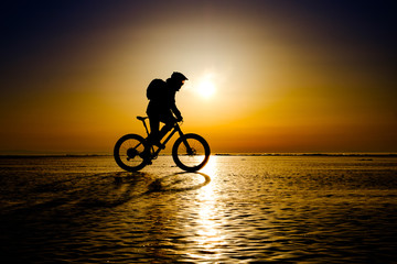 Fototapeta na wymiar Silhouette of bicyclist riding on the clear ice surface of frozen lake in morning backlight