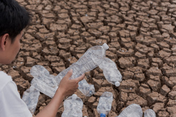 An Asian man hand picking up bottle plastic in arid soil. Concept of environmental protection against global warming