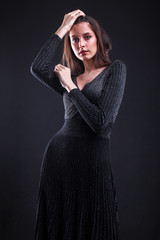 Portrait of a young brunette girl in black tight dress on a black wall backgroundll