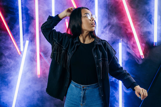 Fashion portrait of young elegant woman in sunglasses in a black T-shirt on a neon background in smoke