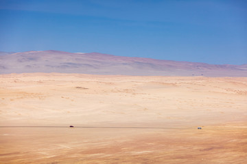 View of the desert, in the distance two cars go on the road, Paracas National Reserve.