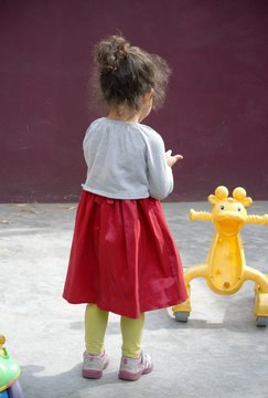 Single Child Girl From Back With Red Dress Playing With Yellow Toy