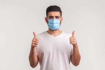 Effective protection against contagious disease. Man showing thumbs up and wearing hygienic mask to...