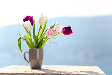 Spring flowers on balcony at blue background of mountains. Tulips on wooden table outdoors. Still life at sea beach. Blooming Pink, white, purple bouquet. Copy space.