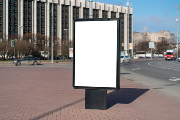 A vertical city billboard standing in a square lit by the sun on a nice weather day. With a white space for posters copy space