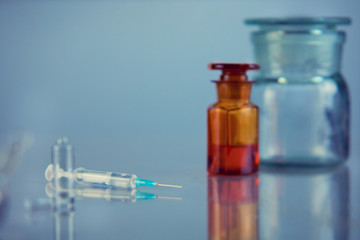 A medical ampoule with a syringe lies on a mirror table, on a blue background